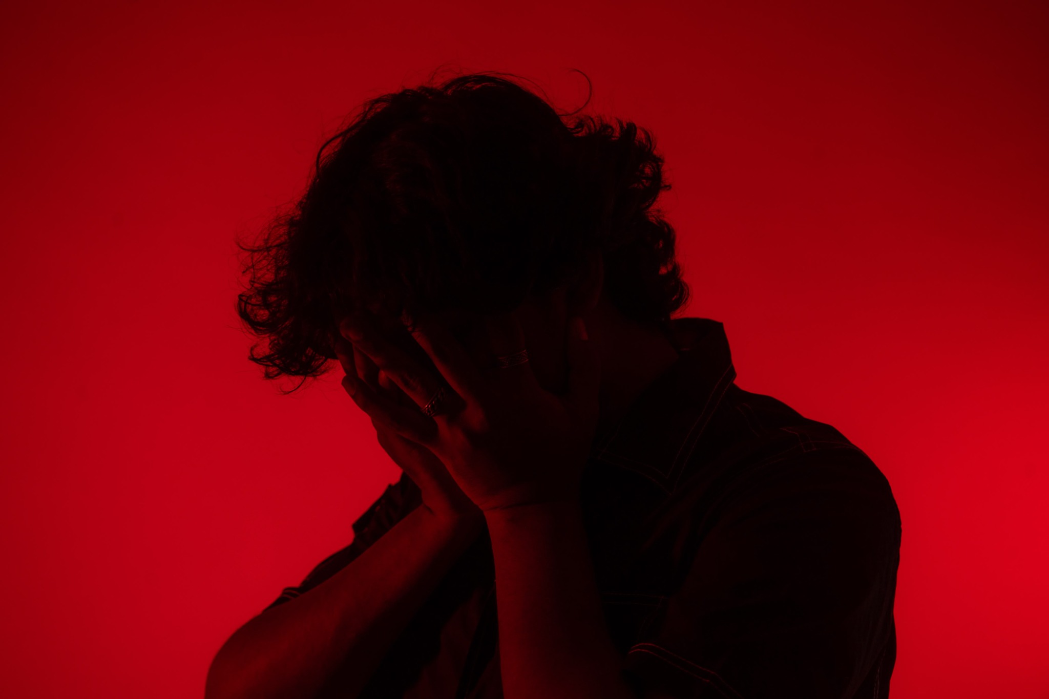 Devoid with his hands covering his face against a vivid red backdrop